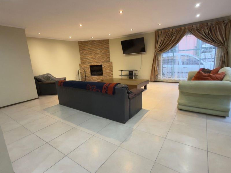 Spacious living room featuring large format floor tiles, recessed downlighting, and a feature stone-clad fireplace, offering a bright and open living environment.