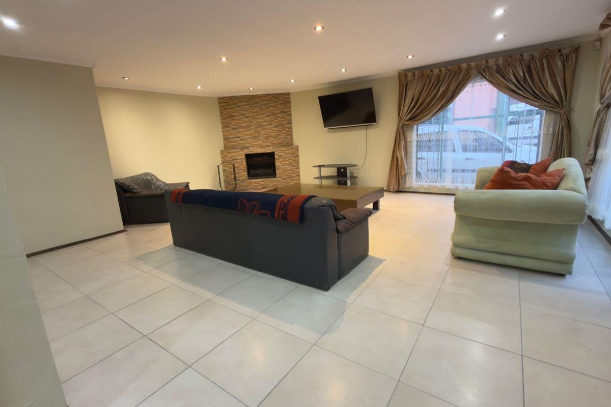 Spacious living room featuring large format floor tiles, recessed downlighting, and a feature stone-clad fireplace, offering a bright and open living environment.