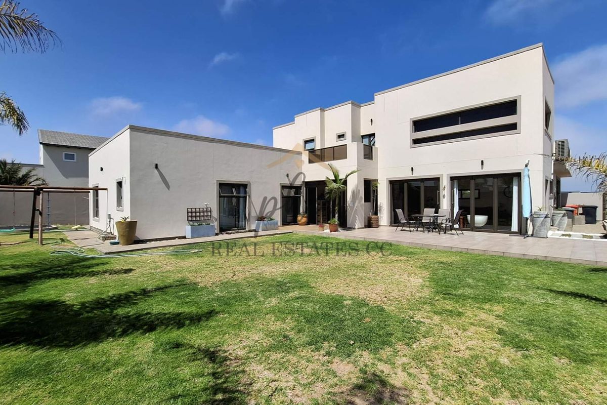 Rear view of a modern two-story house featuring a spacious tiled patio, large sliding glass doors, and a well-maintained lawn.