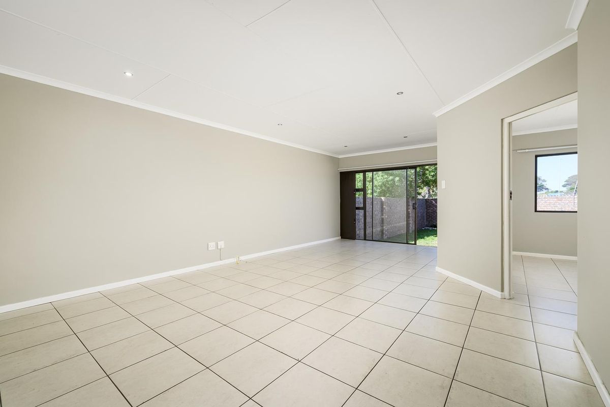 Spacious, light-filled living area featuring neutral tiled flooring, recessed ceiling lighting, and sliding glass doors providing direct access to the rear garden.