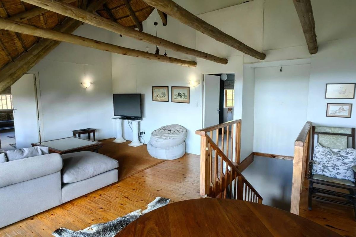 Spacious loft living area featuring exposed timber roof trusses, a traditional thatched ceiling, and polished wooden flooring with an open staircase.