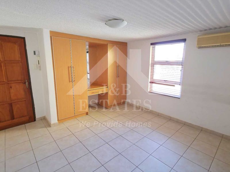 A spacious bedroom featuring built-in cupboards, tiled flooring, and an integrated air conditioning unit, offering a functional and neutral living space.