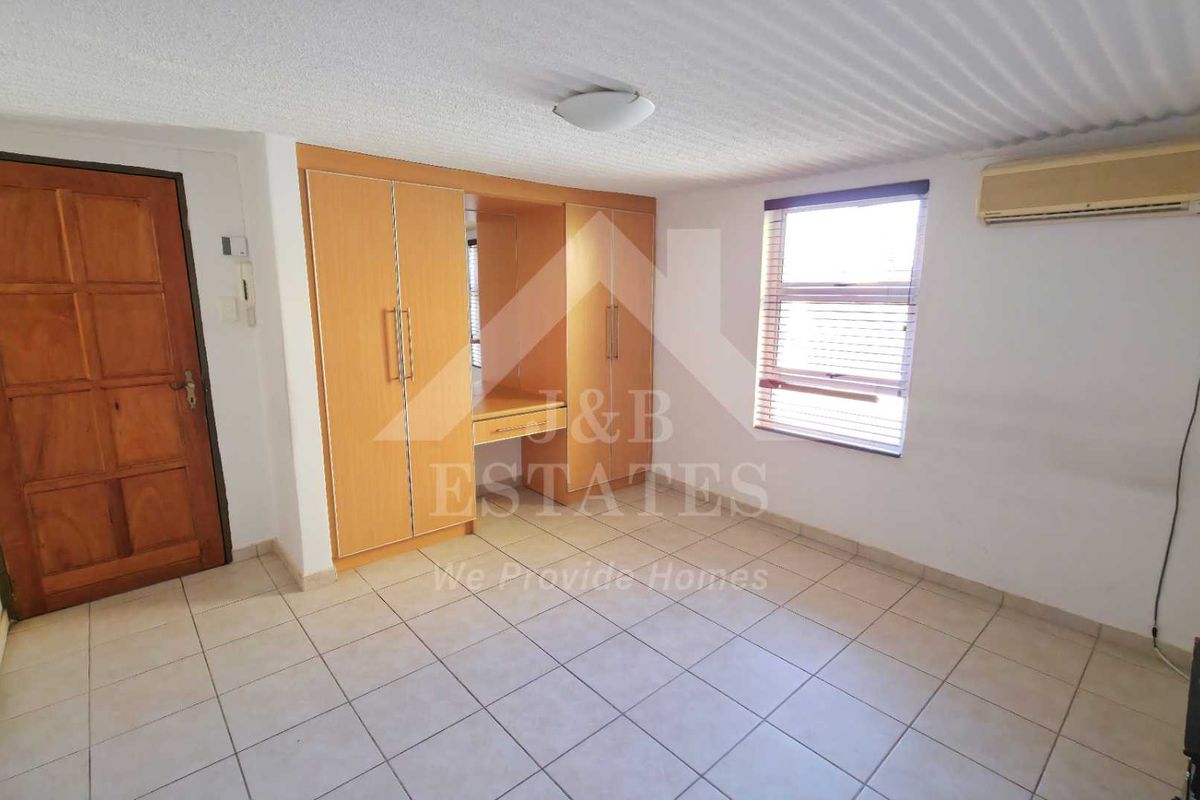 A spacious bedroom featuring built-in cupboards, tiled flooring, and an integrated air conditioning unit, offering a functional and neutral living space.