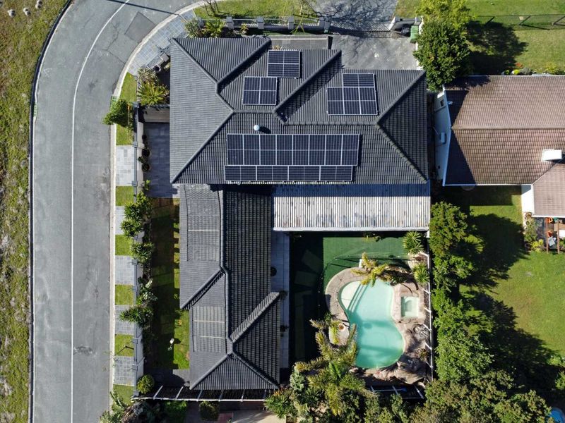 Aerial view of a residential property featuring a tiled roof with solar panels, a swimming pool with integrated spa, and landscaped garden areas.