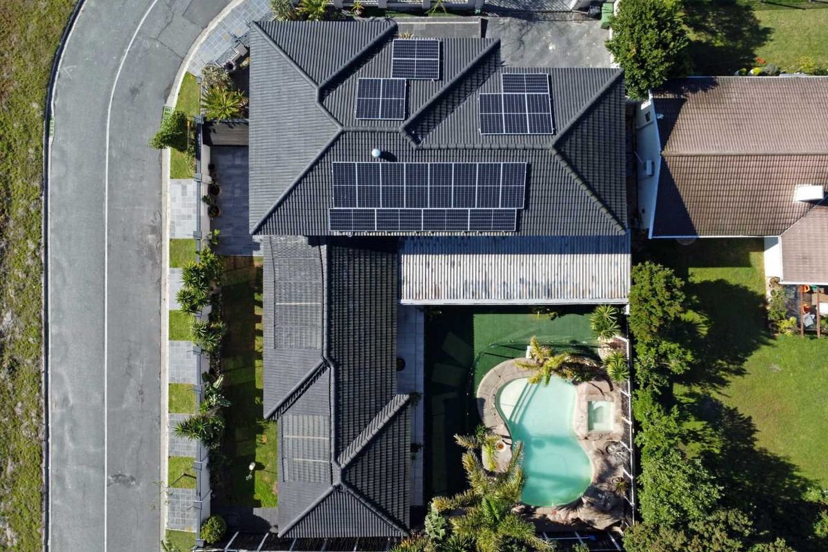 Aerial view of a residential property featuring a tiled roof with solar panels, a swimming pool with integrated spa, and landscaped garden areas.
