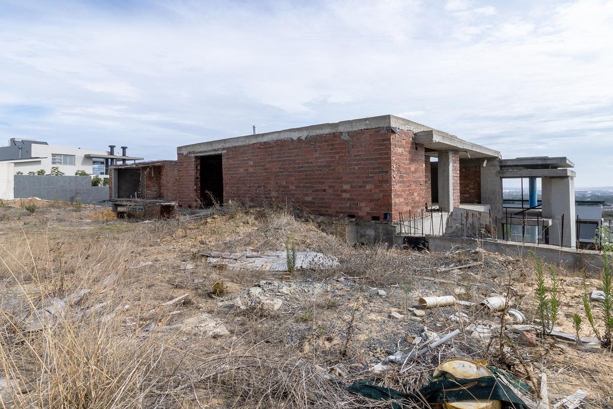 An unfinished residential construction project featuring exposed brick and concrete structural elements on a large, undeveloped plot.