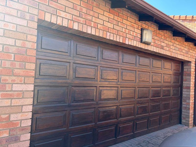 A view of a residential garage featuring a dark wood-finish sectional door set within a face-brick exterior wall.