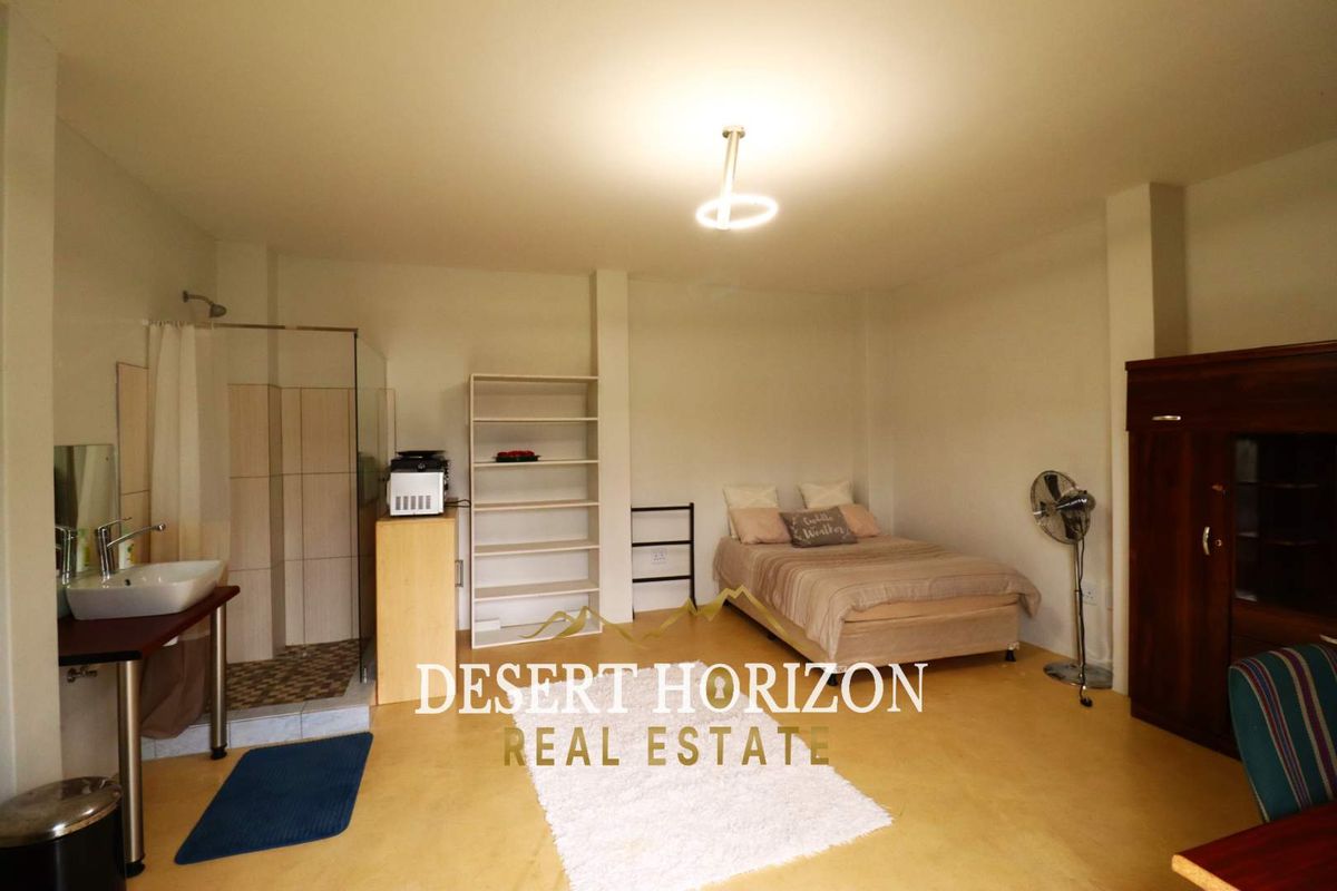 Open-plan studio bedroom featuring an integrated shower cubicle and vanity basin, offering a functional living space.