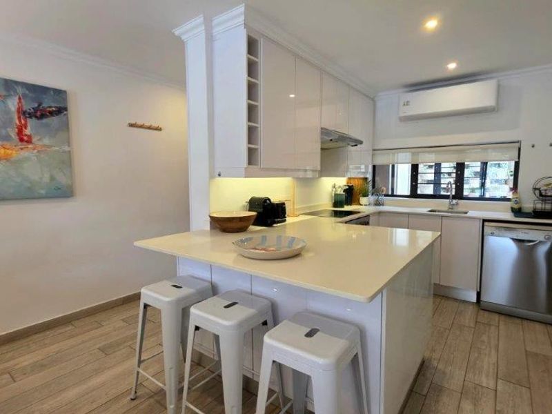 Modern kitchen featuring glossy white cabinetry, quartz countertops, an integrated breakfast bar, and tiled flooring, complemented by under-cabinet lighting and a split-system air conditioner.
