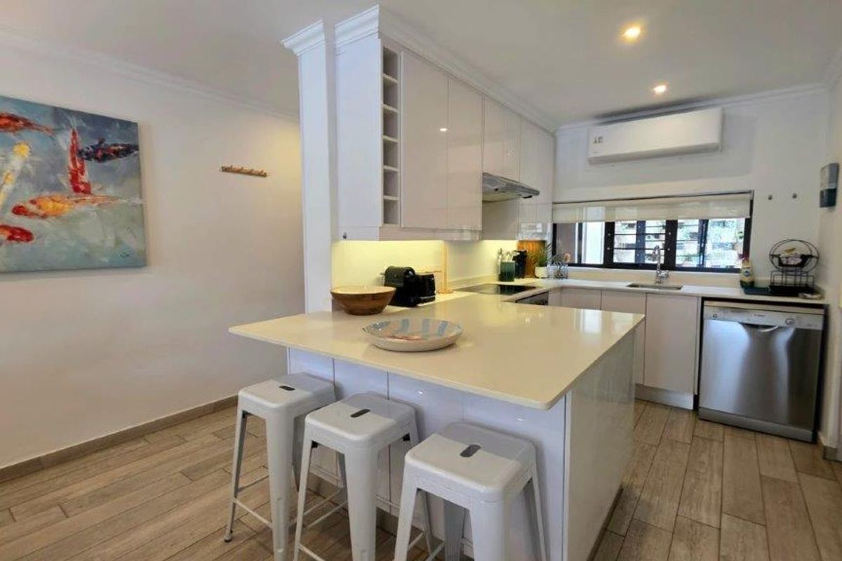 Modern kitchen featuring glossy white cabinetry, quartz countertops, an integrated breakfast bar, and tiled flooring, complemented by under-cabinet lighting and a split-system air conditioner.