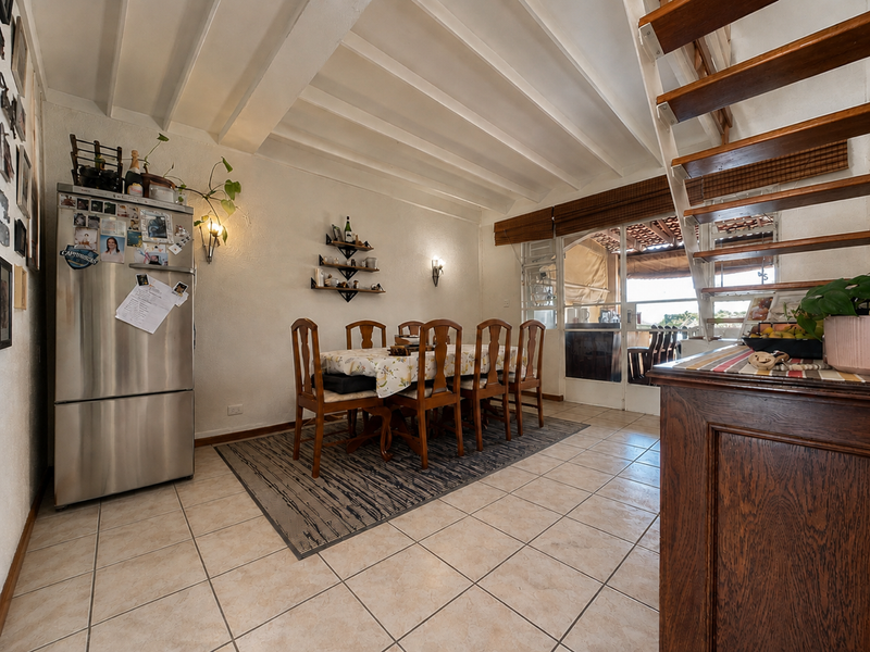 Open plan dining area featuring exposed beam ceilings, ceramic tiled flooring, and a timber staircase leading to the upper level with access to a patio.