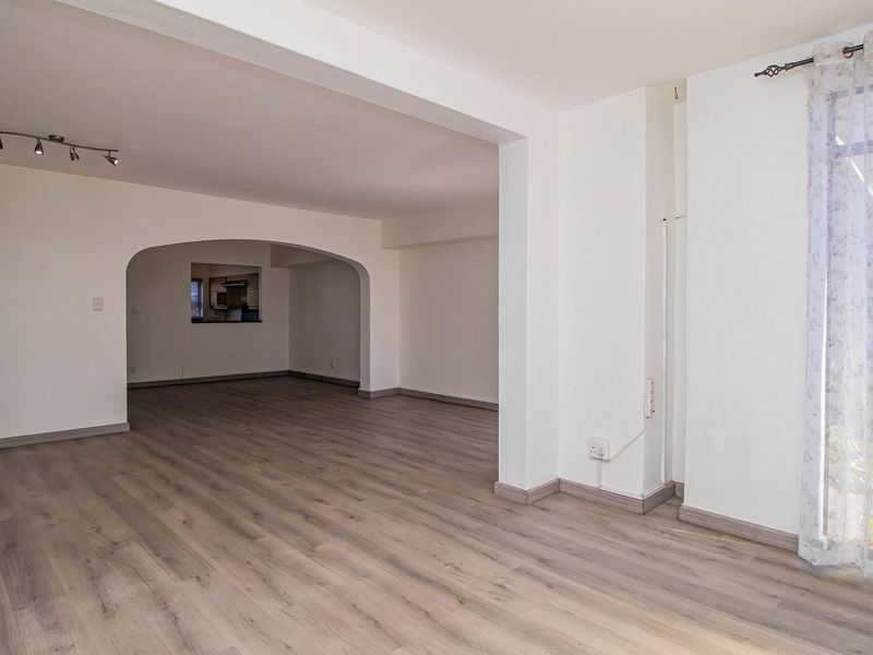 Spacious open-plan living area featuring modern laminate flooring, neutral walls, and a distinctive architectural archway connecting to the adjacent space.