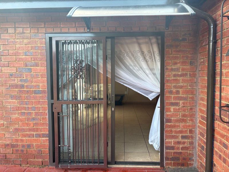Exterior view of a rear entrance featuring a sliding glass door with a security gate and a protective awning over the brick facade.
