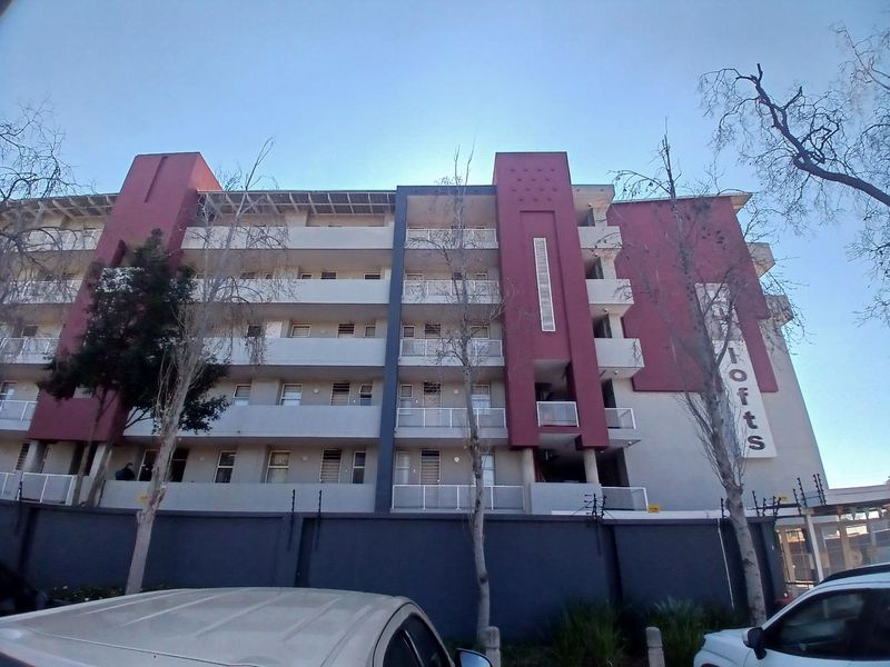 Exterior view of a multi-story apartment building featuring balconies, a perimeter wall with electric fencing, and a secure entrance.