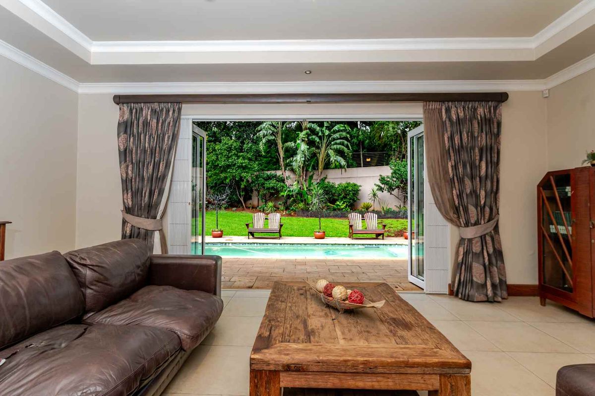 Spacious living room featuring large bi-fold doors that open onto a paved patio, swimming pool, and lush garden area.