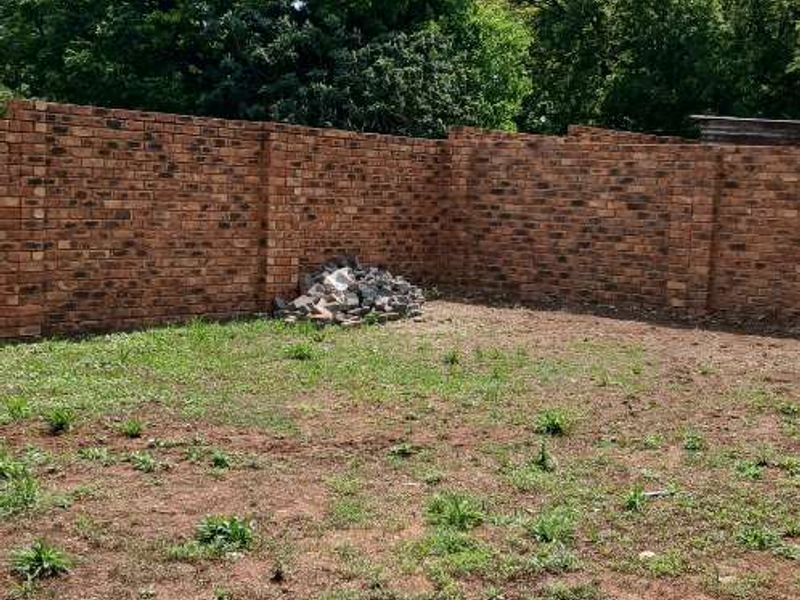 A spacious backyard area enclosed by a brick perimeter wall, featuring an unlandscaped ground surface and a small pile of construction debris.