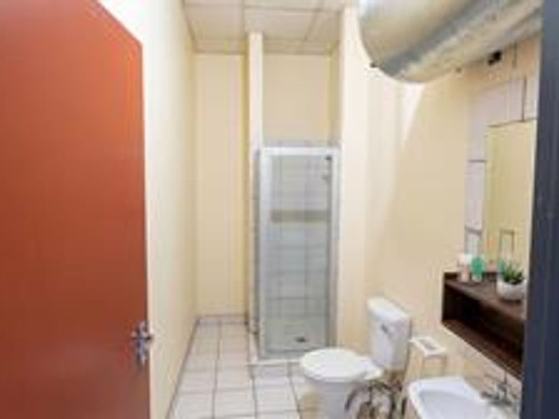 A functional bathroom featuring a shower enclosure, toilet, and washbasin, with exposed water heater and dated finishes, offering potential for modernization.