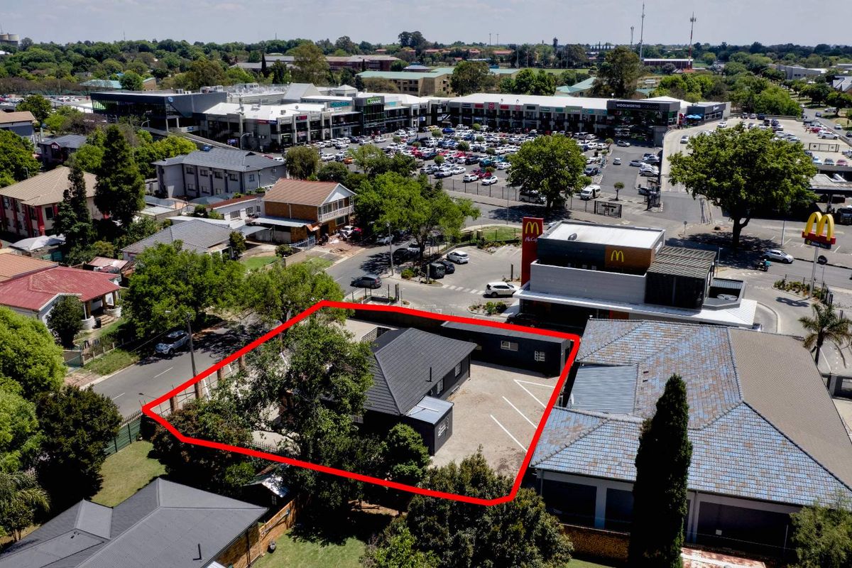 Aerial view of a commercial property featuring a building with a pitched roof and an adjacent asphalt parking area in a busy retail location.