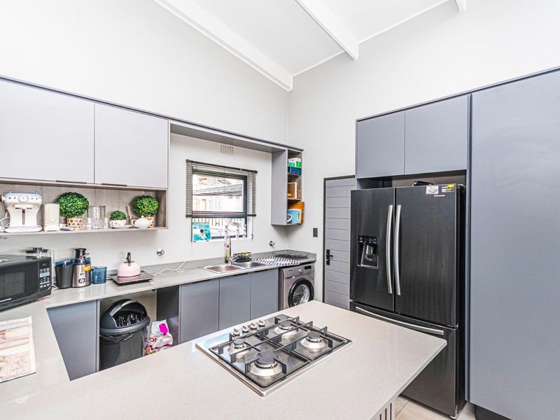 Modern kitchen featuring sleek grey cabinetry, stone countertops, a central island with a gas cooktop, and high vaulted ceilings with exposed beams.