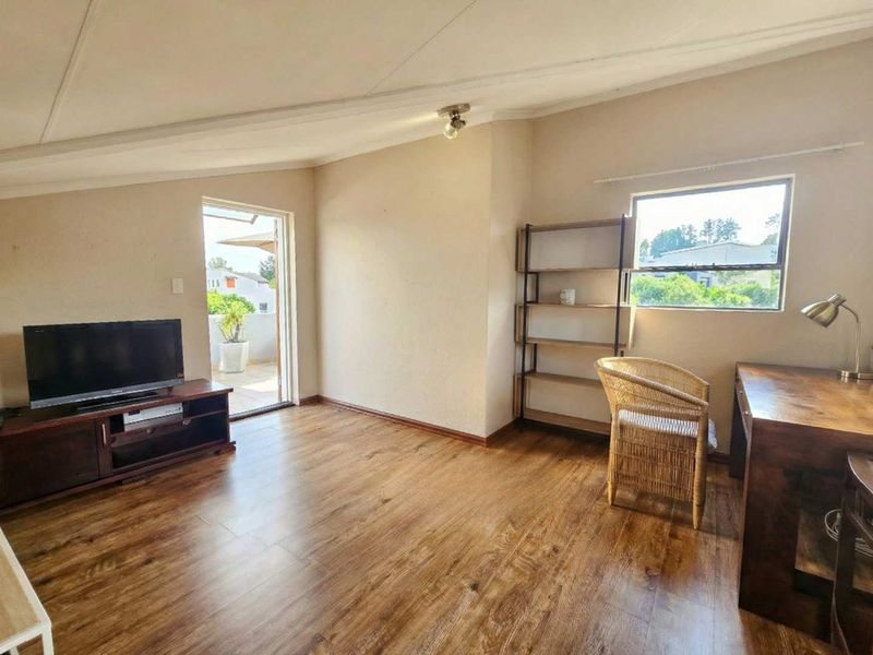 A living area featuring laminate flooring, a sloped ceiling, and direct access to an outdoor balcony through a sliding glass door.