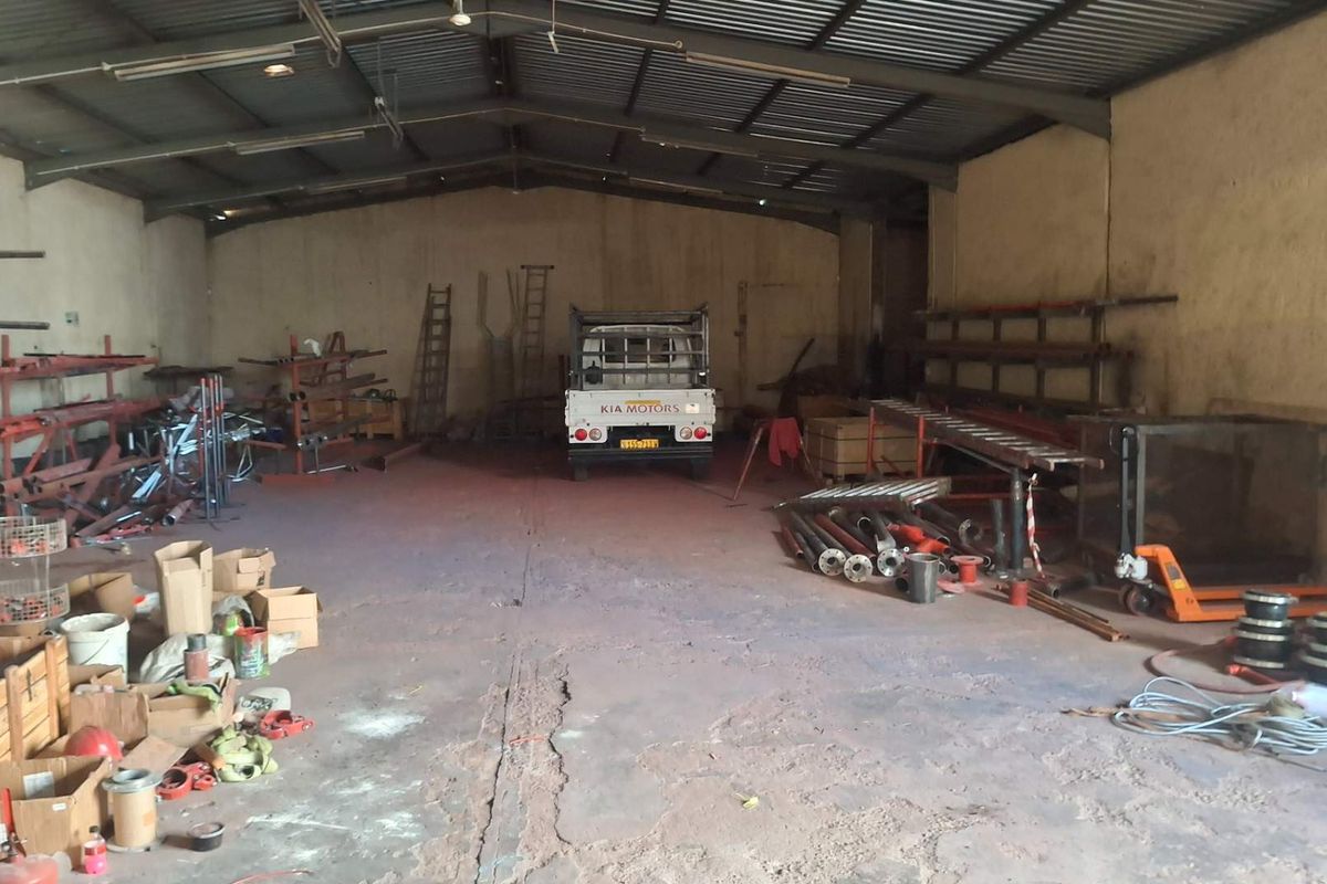 Spacious industrial utility area featuring high ceilings with exposed steel trusses, concrete flooring, and fluorescent lighting, suitable for storage or workshop operations.