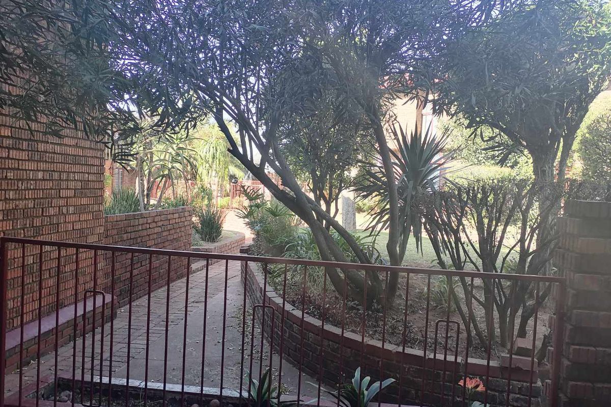A view of the rear exterior area featuring a brick retaining wall, paved walkway, and established garden landscaping enclosed by a metal security railing.