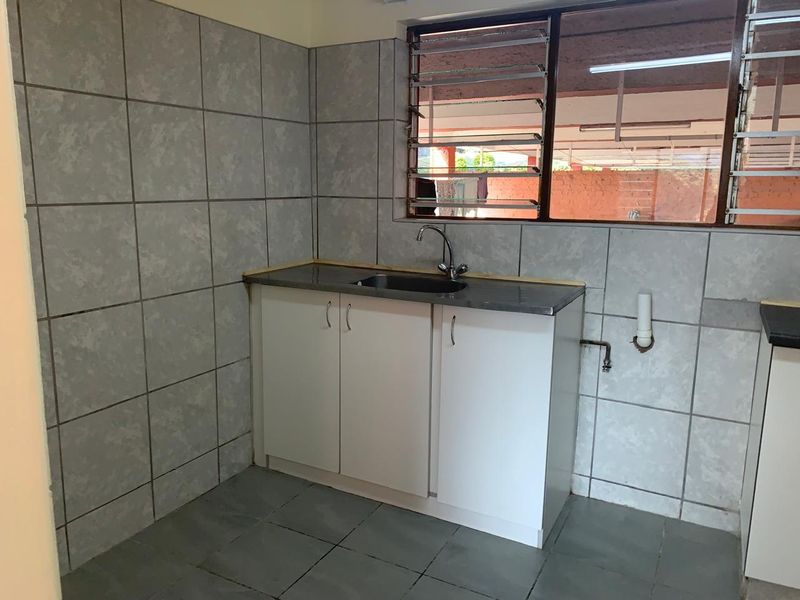 A functional scullery or utility area featuring a stainless steel sink, built-in cabinetry, and tiled wall finishes with louvered windows.