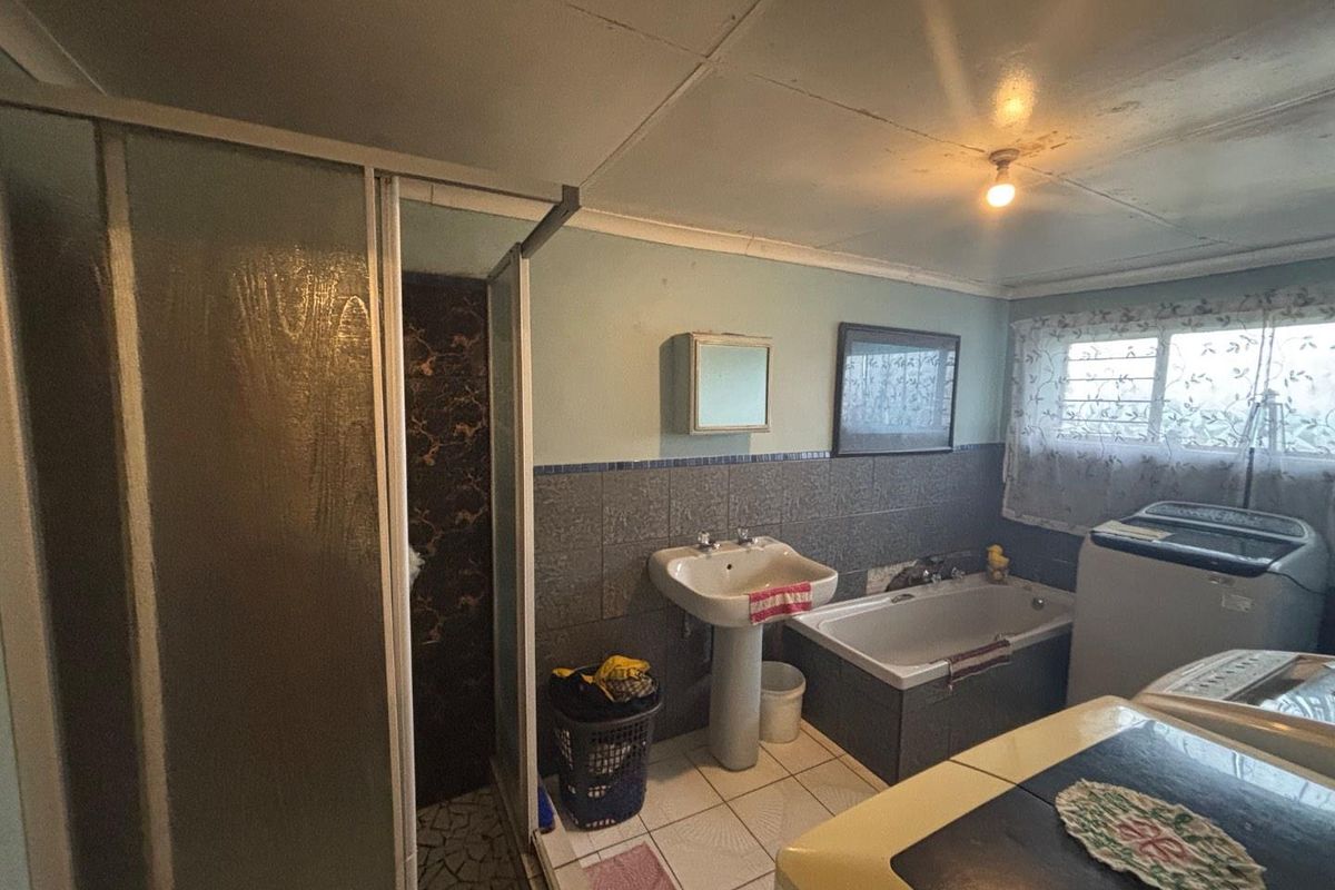 A functional bathroom featuring a pedestal basin, a built-in bathtub, and a separate shower enclosure with tiled walls and flooring.