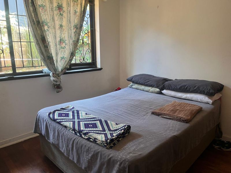 A bedroom featuring timber flooring and a window fitted with security bars.