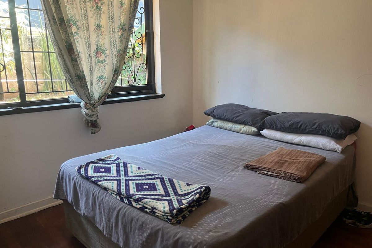 A bedroom featuring timber flooring and a window fitted with security bars.