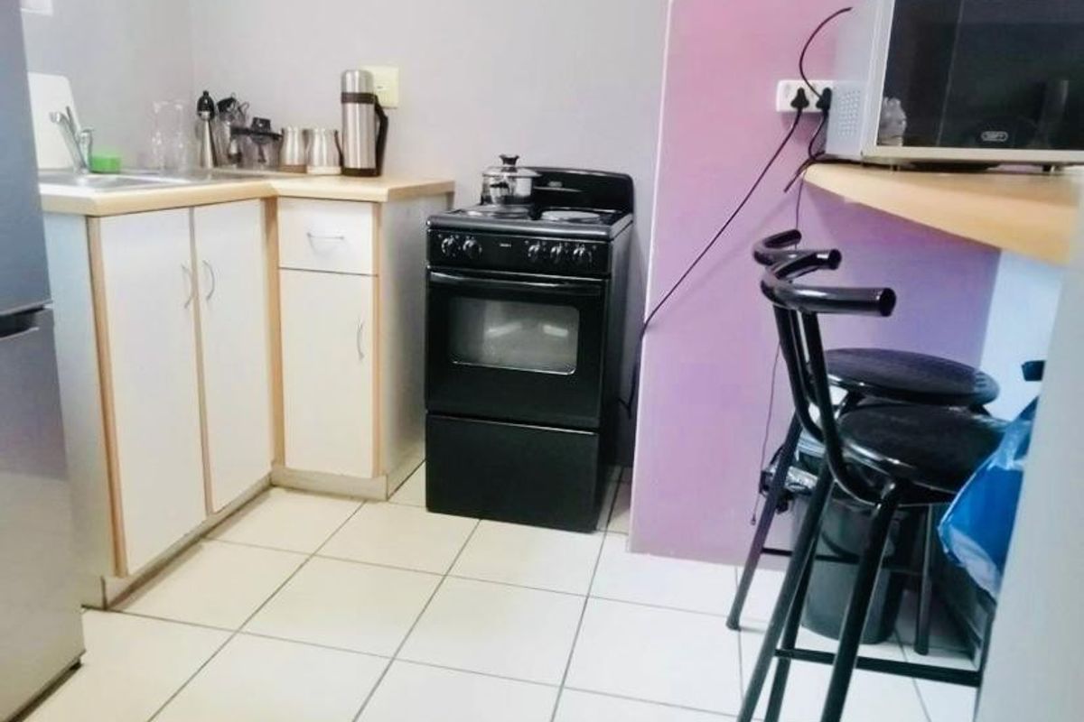 A compact kitchen featuring white cabinetry, a freestanding stove, and tiled flooring with a breakfast bar area.
