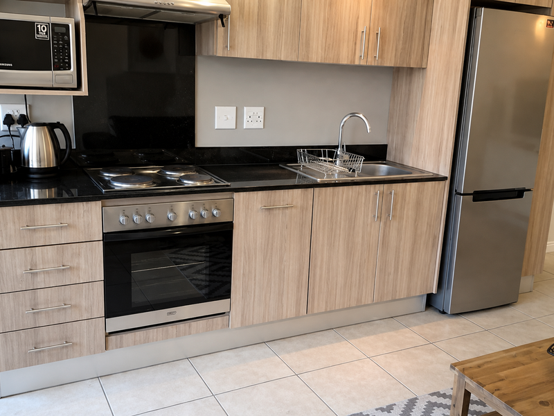Modern kitchen featuring light wood-grain cabinetry, black granite countertops, integrated appliances, and neutral tiled flooring.