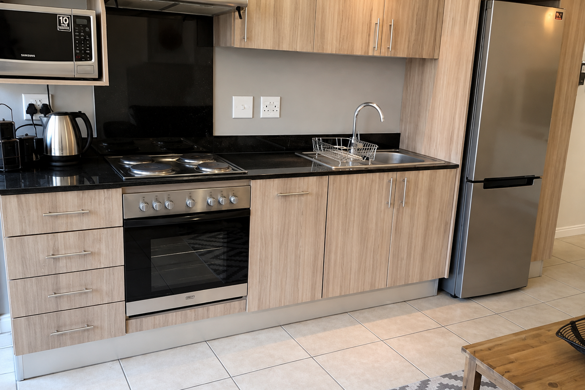 Modern kitchen featuring light wood-grain cabinetry, black granite countertops, integrated appliances, and neutral tiled flooring.