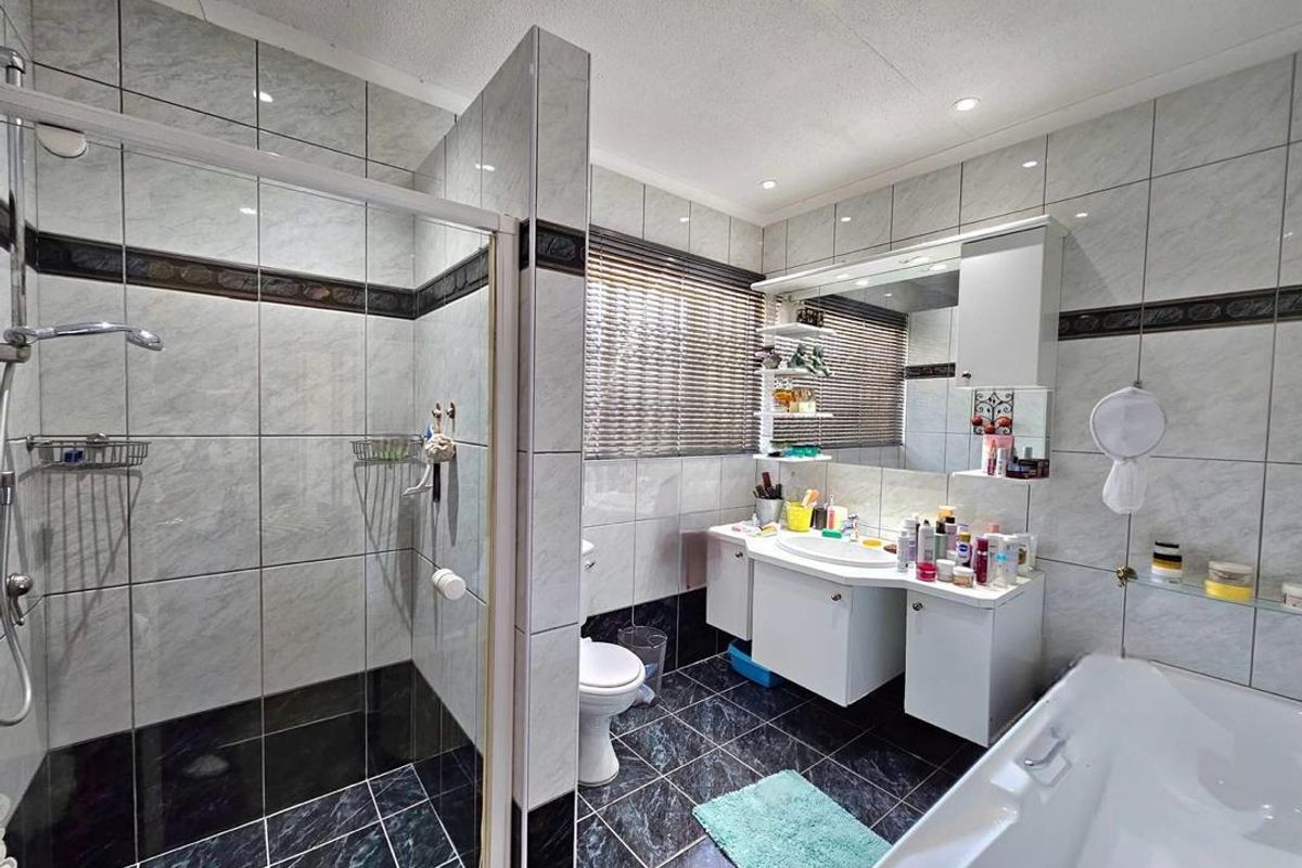A functional bathroom featuring a glass-enclosed shower, a separate bathtub, and a built-in vanity unit with integrated mirror and storage.