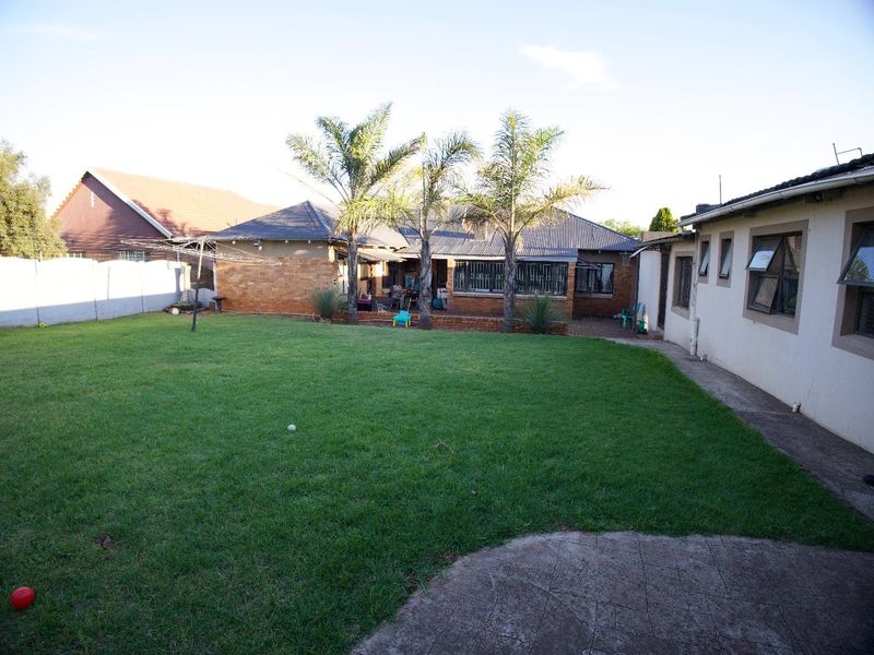 Spacious rear garden featuring a well-maintained lawn, brick facade, and a concrete patio area, providing a functional outdoor space for the property.