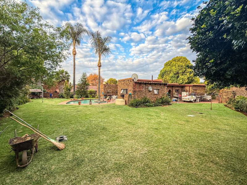 Spacious rear garden featuring a swimming pool, paved patio area, and established landscaping with mature palm trees.