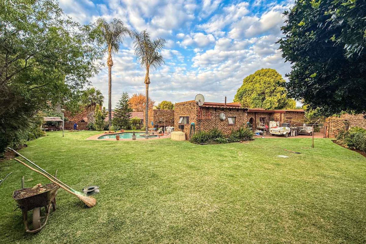 Spacious rear garden featuring a swimming pool, paved patio area, and established landscaping with mature palm trees.