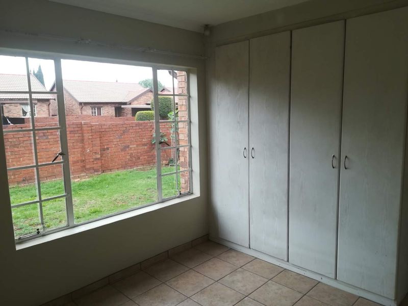 A vacant bedroom featuring tiled flooring, built-in cupboards, and a large window overlooking the rear garden area.