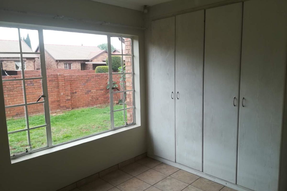 A vacant bedroom featuring tiled flooring, built-in cupboards, and a large window overlooking the rear garden area.