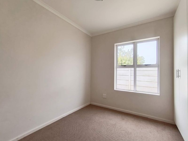 A clean, neutral-toned bedroom featuring built-in cupboards, carpeted flooring, and a window providing natural light.
