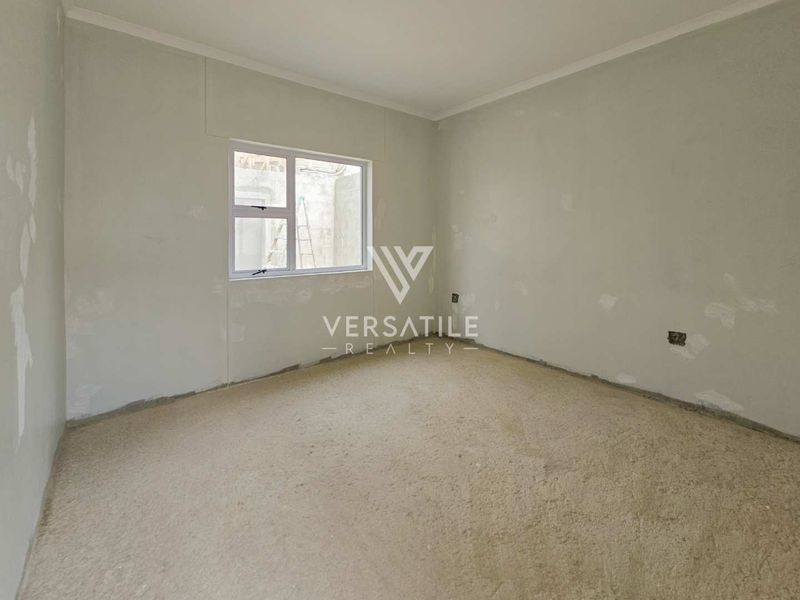 An empty bedroom featuring unfinished wall surfaces, carpet flooring, and an aluminium window frame, offering a blank canvas for renovation.