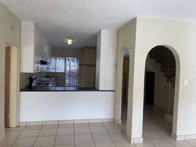 Open plan kitchen area featuring built-in cabinetry, stove, and tiled flooring, connected to a hallway with an archway and staircase.