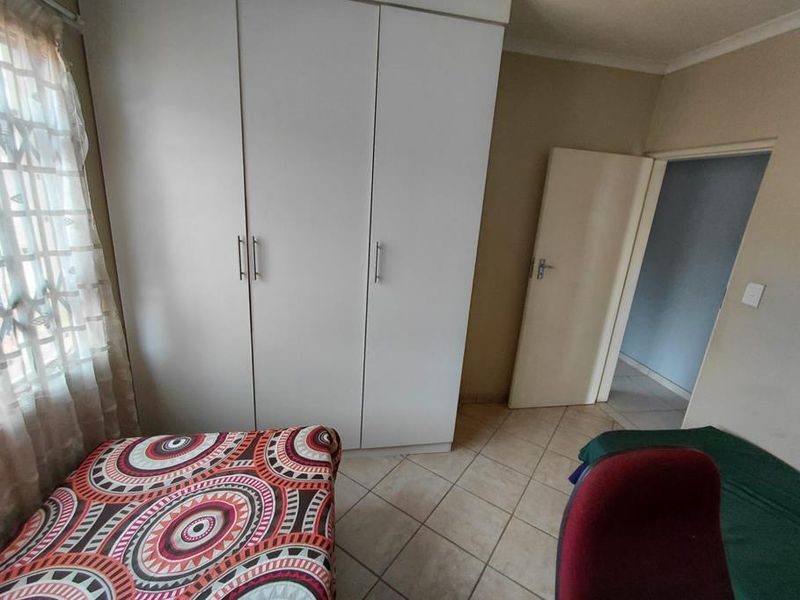 A bedroom featuring tiled flooring and a built-in white wardrobe, providing functional storage space.
