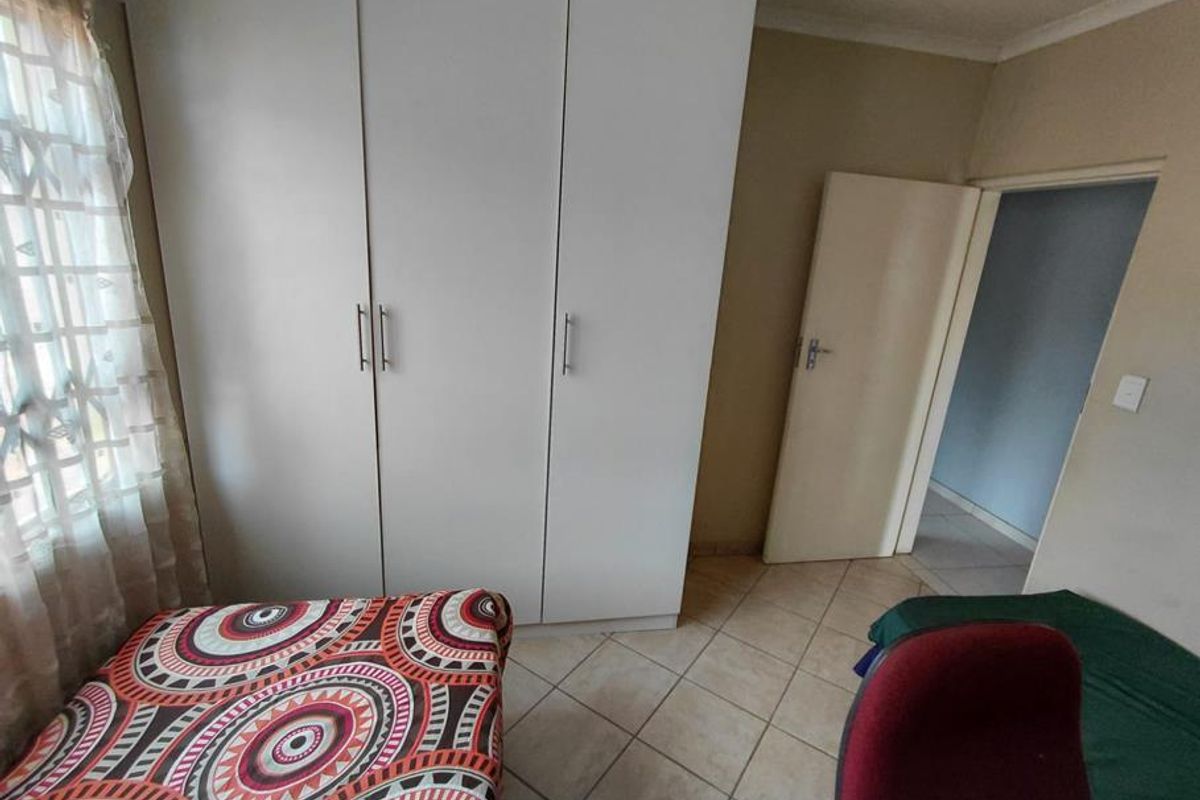 A bedroom featuring tiled flooring and a built-in white wardrobe, providing functional storage space.