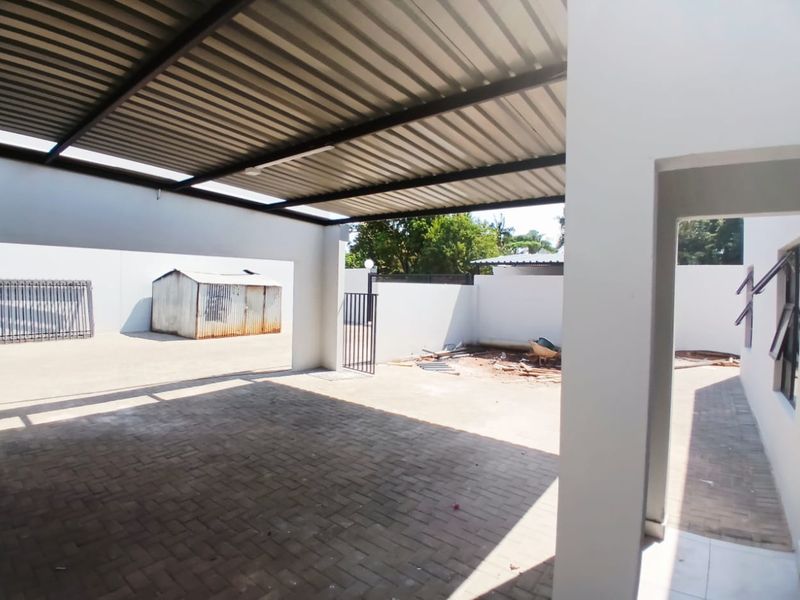 A covered outdoor patio area featuring paved flooring and a metal roof structure, adjacent to an unfinished yard space.