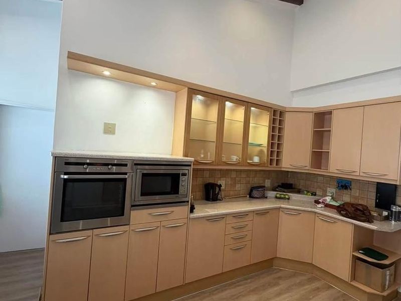 A well-maintained kitchen featuring light wood cabinetry, built-in oven and microwave, tiled backsplash, and exposed ceiling beams with recessed lighting.