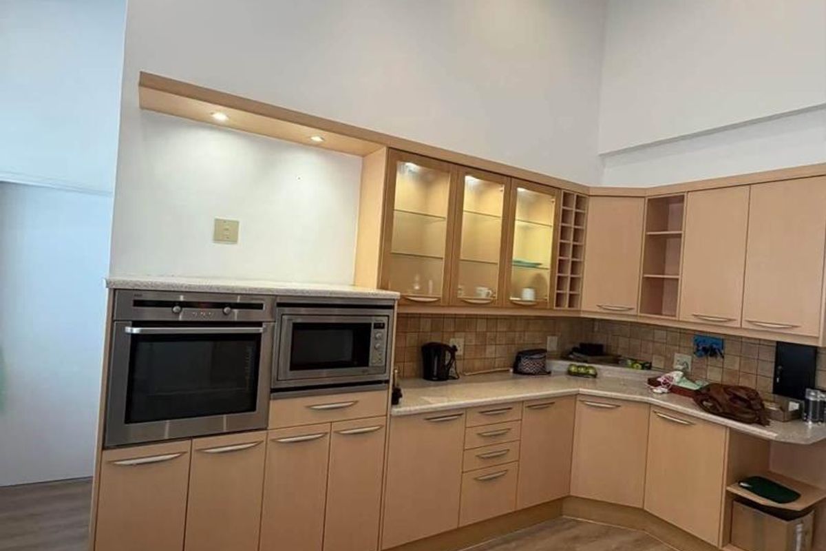 A well-maintained kitchen featuring light wood cabinetry, built-in oven and microwave, tiled backsplash, and exposed ceiling beams with recessed lighting.