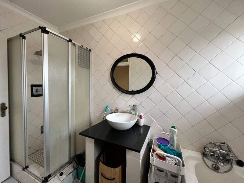 A functional bathroom featuring a shower enclosure, a vanity basin with a black countertop, and a bathtub with tiled wall finishes.