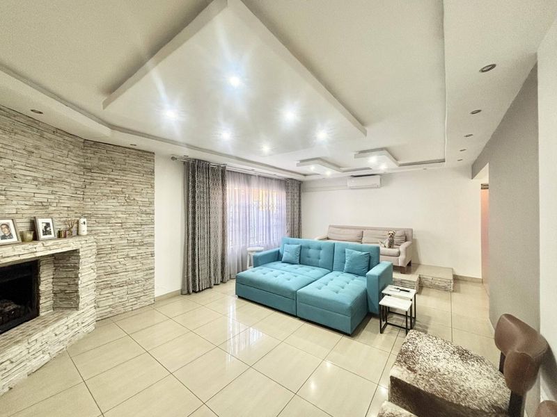 Spacious living room featuring a stone-clad fireplace, modern recessed ceiling lighting, tiled floors, and a wall-mounted air conditioning unit.