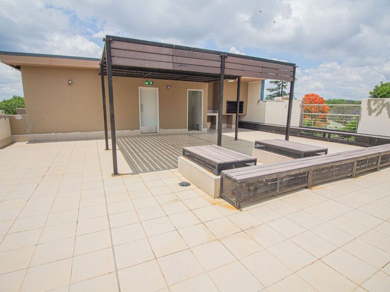 Spacious rooftop patio featuring a pergola, built-in braai, and integrated seating, offering an ideal outdoor entertainment area for the apartment.